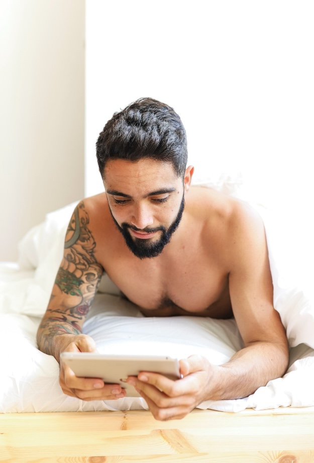 Man laying down on his stomach and looking at a tablet after his gynecomastia surgery