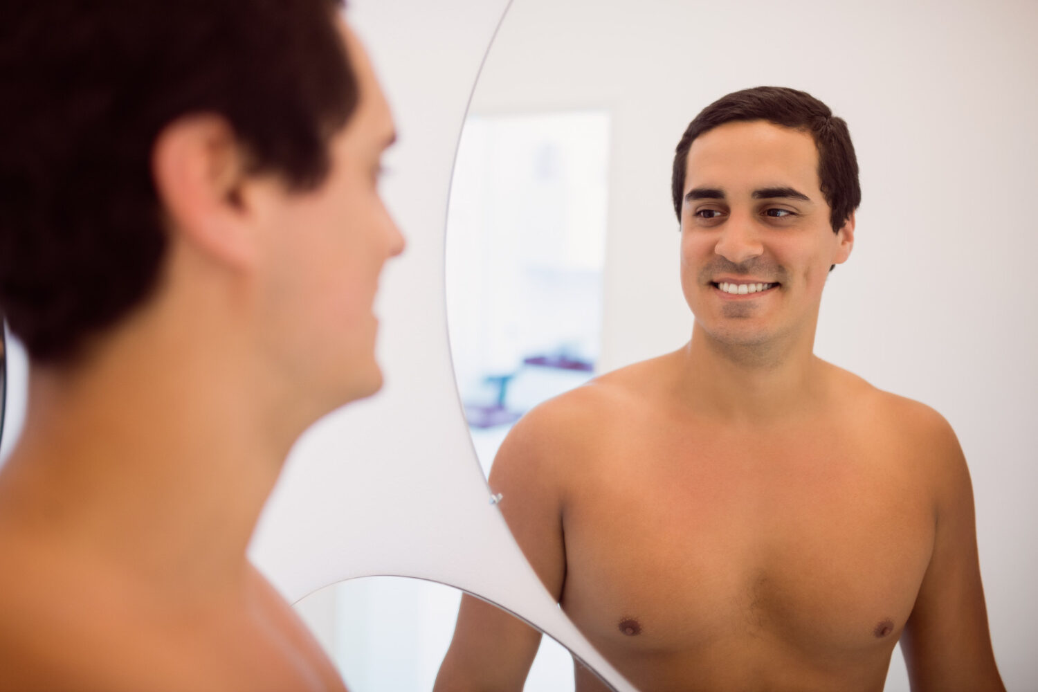 man looking confidently in the mirror and at himself after a male breast reduction surgery