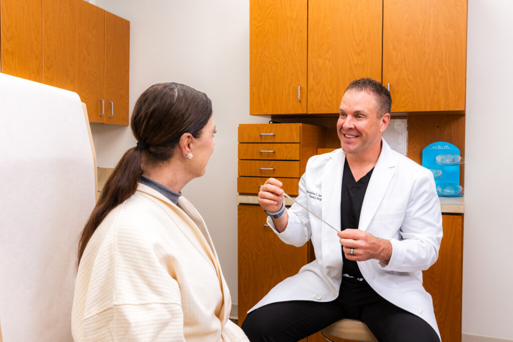 Dr. Specht is speaking with a female patient about the skin treatments we offer in Indianapolis. They are sitting in a private room, the patient has long brown hair in a ponytail and Dr. Specht is kindly smiling at her as he explains the treatments.