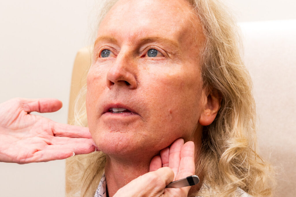 Patient looking up while their provider places hands along their jawline and neck to assess their facial structure.
